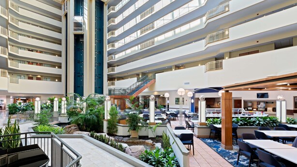 Un vestíbulo de hotel de varios niveles con un atrio central, varias zonas de comedor y una escalera que conecta los pisos.