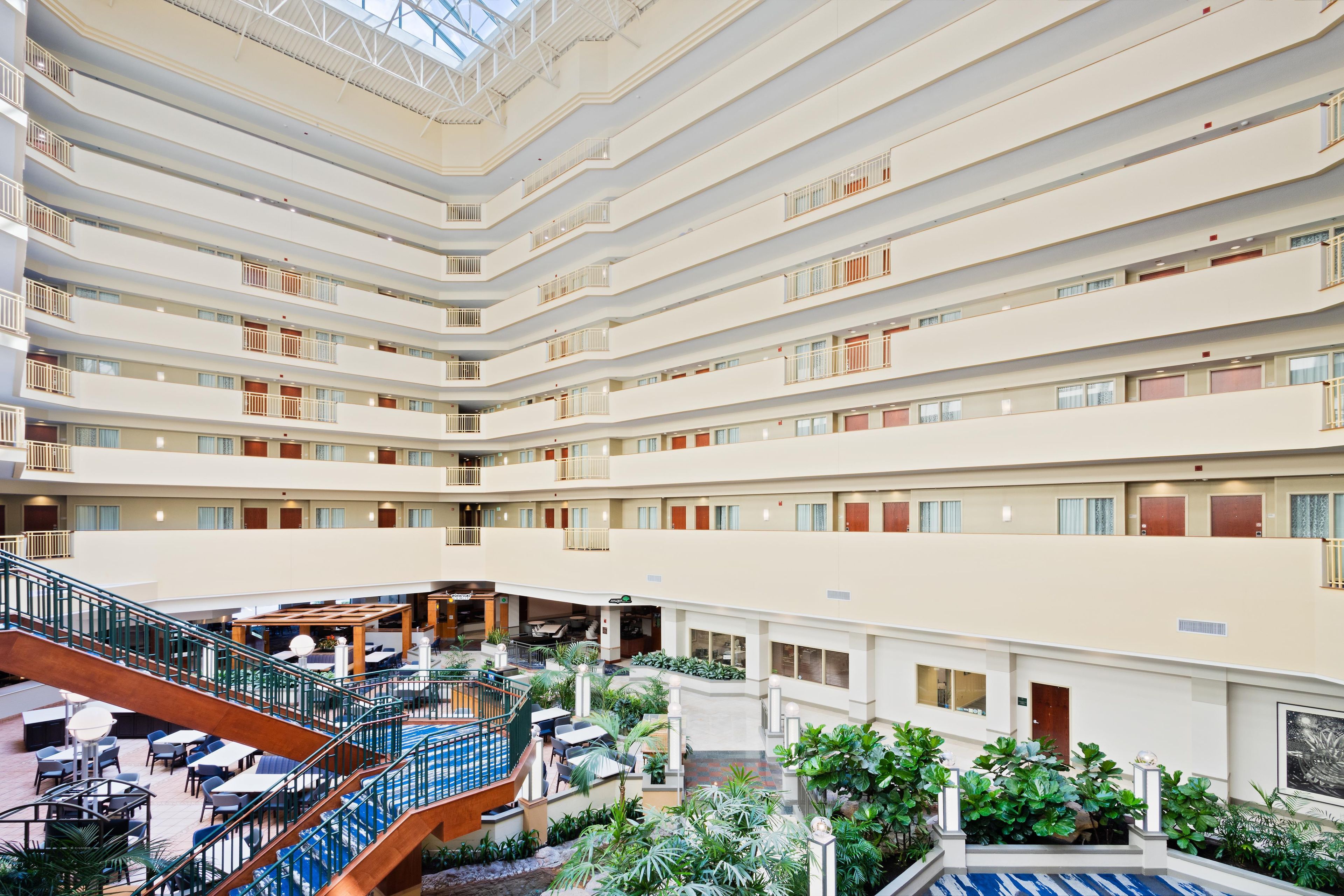 Een hotelatrium met meerdere niveaus, een centrale trap, een terras buiten en veel groen.