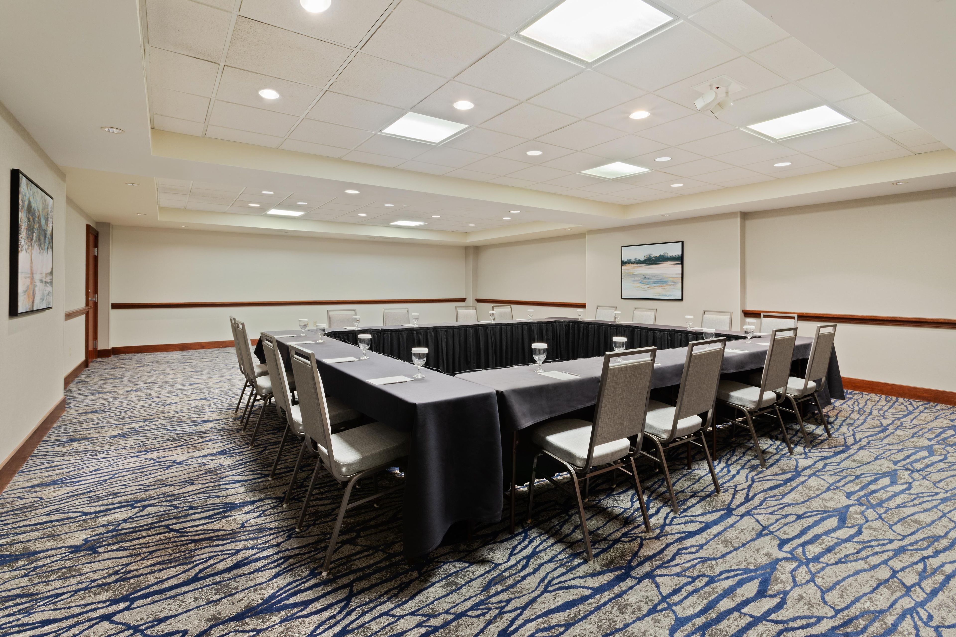 Un salón de conferencias con una mesa larga, sillas y suelo alfombrado.