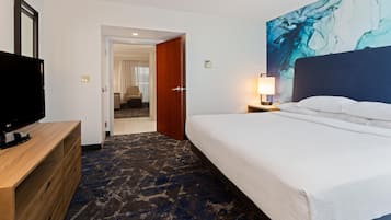A hotel room with a bed, a TV, a desk, and a painting on the wall.