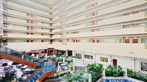 Un vestíbulo de hotel de varios niveles con balcones, zonas de estar interiores y una escalera central.