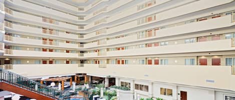 Un vestíbulo de hotel de varios niveles con balcones, zonas de estar interiores y una escalera central.