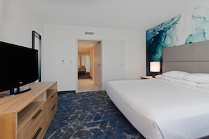 Hotelkamer met een bed, een televisie op een houten standaard, een schilderij aan de muur en een deur naar een andere kamer.