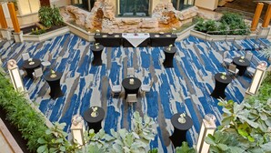 Amplio espacio interior con alfombra azul estampada, varias mesas con sillas y una zona de estar central con mantel blanco.