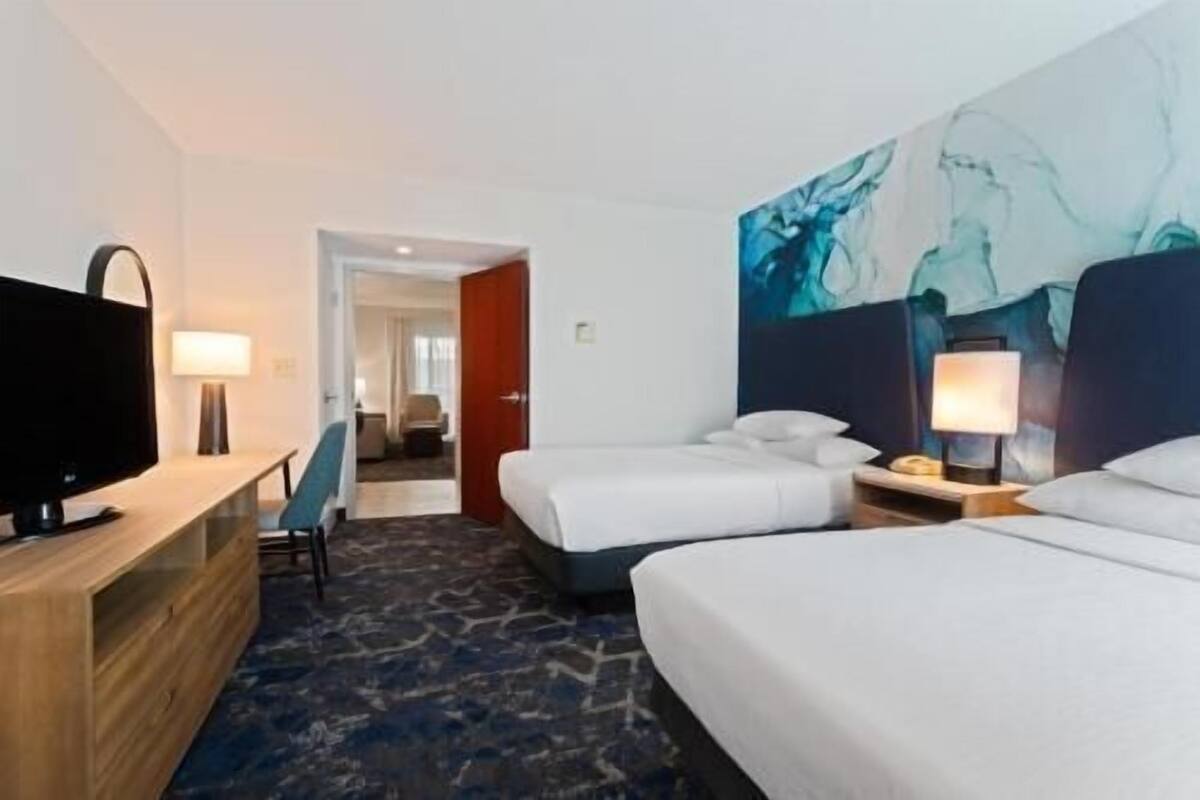 Ein Hotelzimmer mit zwei Betten, einem Fernseher, einem Schreibtisch und einem Bild an der Wand.
