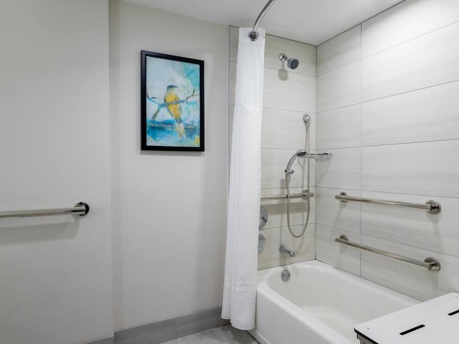 A modern bathroom with a bathtub, shower, and handrails.