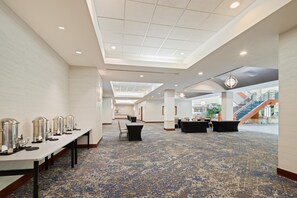 Eine großzügige Hotelhalle mit hoher Decke, einem gemusterten Teppich und einer Sitzecke mit Tischen und Stühlen.