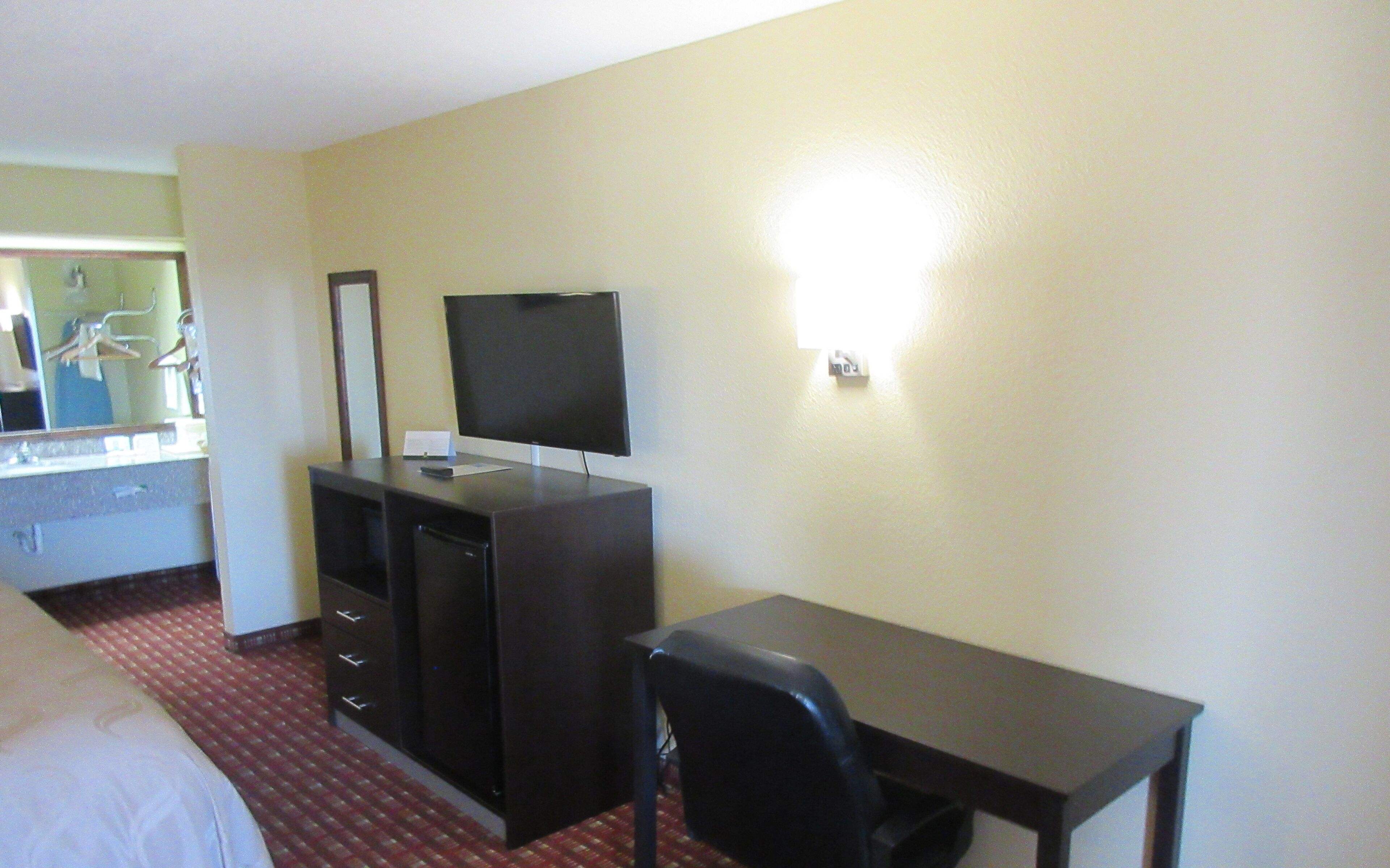A hotel room with a bed, a desk with a chair, a television, and a mirror.