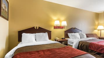 Habitación de hotel con dos camas, cabecera de madera, mesita de noche con teléfono y lámparas fijadas a la pared.