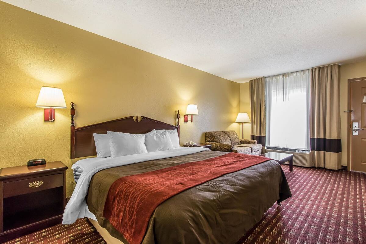 A hotel room with a large bed, two bedside lamps, a nightstand, a chair, and a window with curtains.