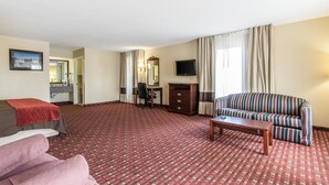 A hotel room with a red patterned carpet, a bed, a pink sofa, a striped sofa, a desk with a chair, a television, and a mirror. - Quality Inn Andalusia (Andalusia)