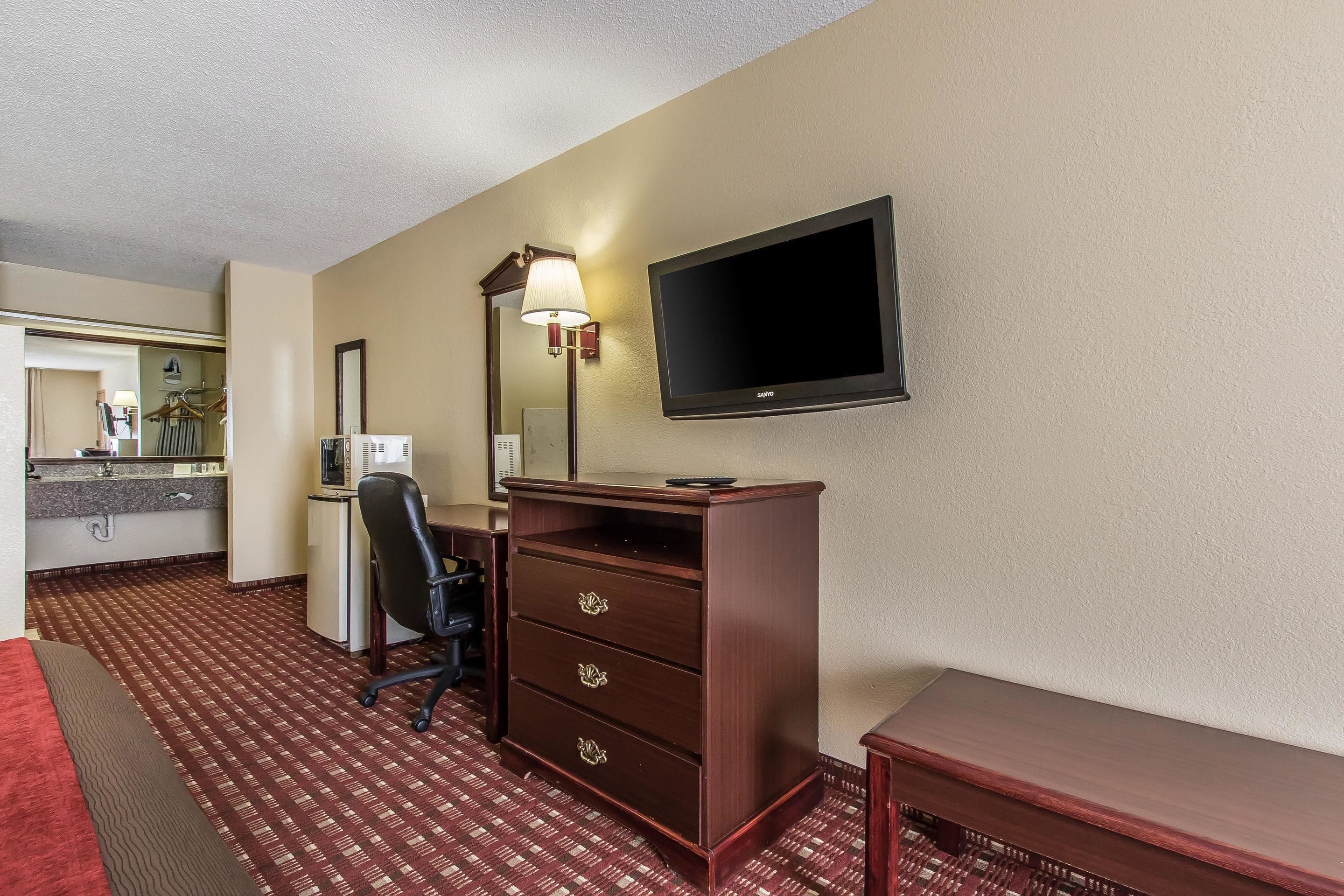 A hotel room with a desk, chair, TV, and a mirror.