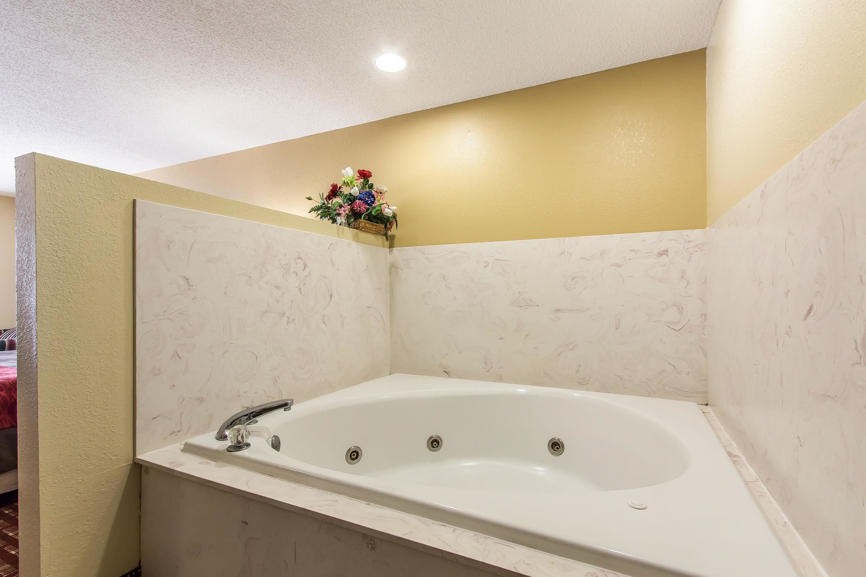 A bathroom with a white bathtub, a small flower arrangement on the wall, and a visible shower area.