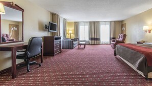 A hotel room with a red carpet, a bed, a desk with a chair, a television, a sofa, and a window with curtains. - Quality Inn Andalusia (Andalusia)