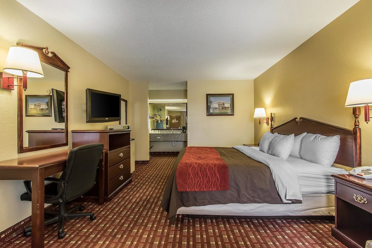 A hotel room with a bed, desk, chair, TV, and a bathroom visible in the background.