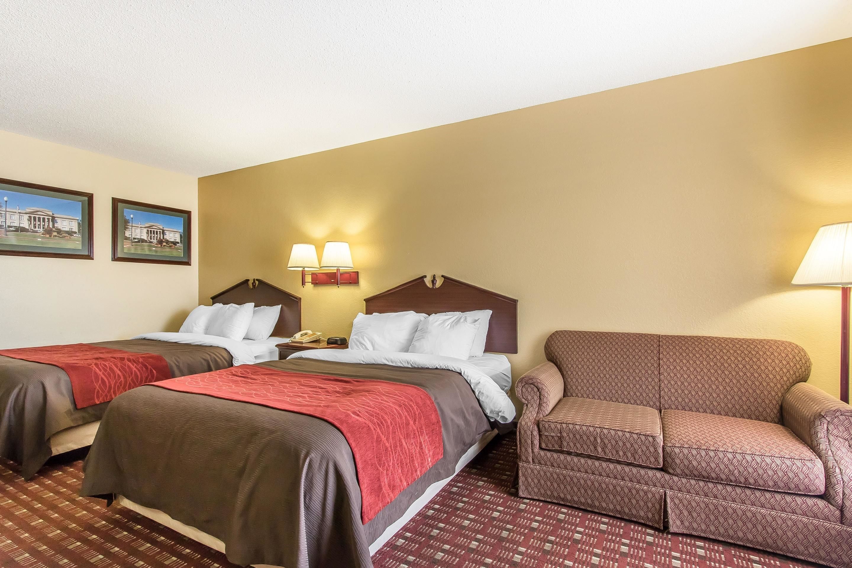 A hotel room with two beds, a sofa, and a nightstand with a lamp.
