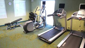 A hotel fitness room with treadmills, an elliptical, dumbbells, and a bench.
