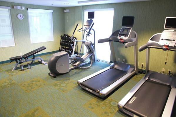 A hotel fitness room with treadmills, an elliptical, dumbbells, and a bench.