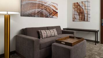 A modern living room with a grey sofa, a small ottoman, a wooden tray, a floor lamp, and two abstract wall art pieces.