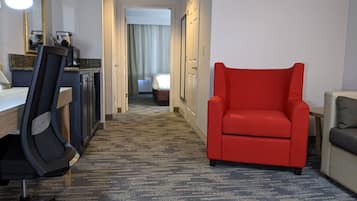 A hotel room with a desk, chair, red armchair, and a bed with a curtain.