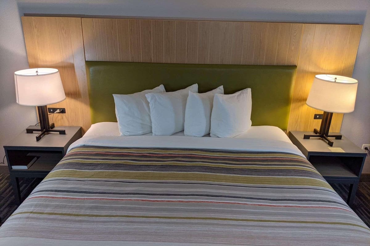 A hotel room with a large bed, two bedside tables with lamps, a wooden headboard, and a striped bedspread.