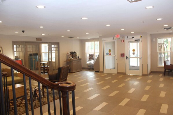 A spacious lobby with a wooden staircase, a reception desk, and a dining area.