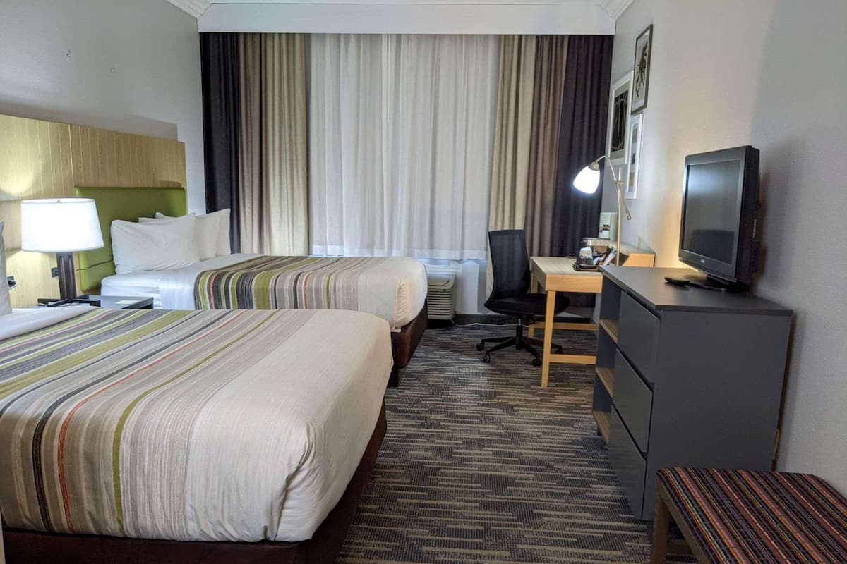 A hotel room with two beds, a desk, a chair, a television, and a lamp.