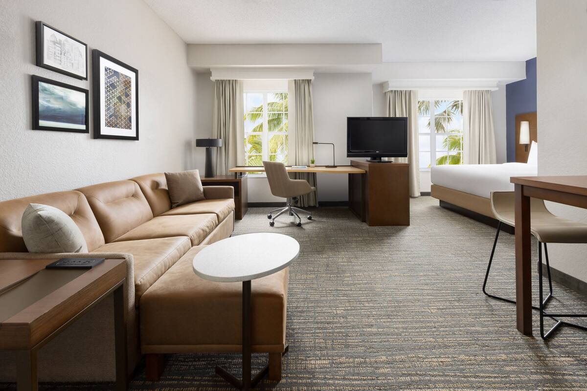 Habitación de hotel con sofá, escritorio, cama, televisor y cuadros en la pared.