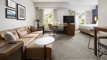 Ein Hotelzimmer mit Sofa, Schreibtisch, Bett, Fernseher und gerahmten Bildern an der Wand.