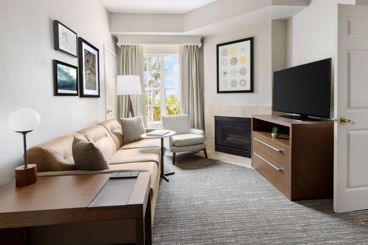 Una habitación de hotel moderna con sofá, sillón, televisor, chimenea y obras de arte en las paredes.