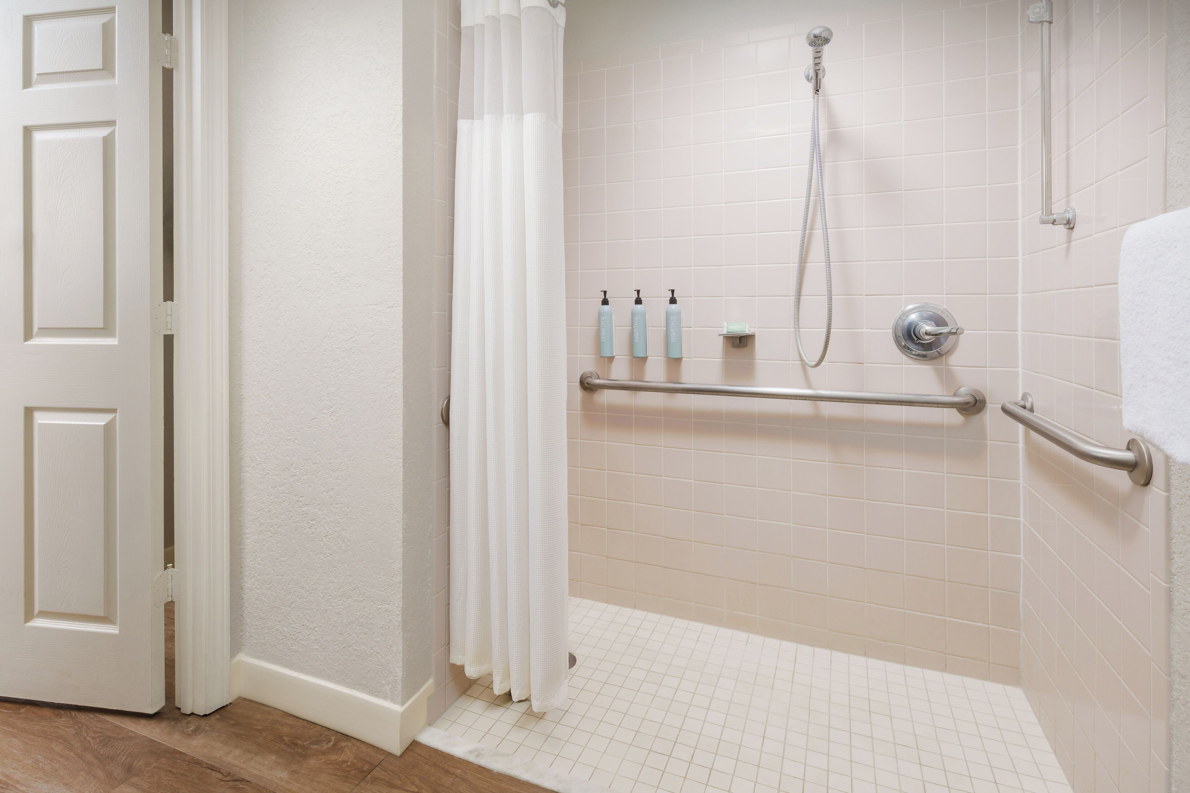 A bathroom with a shower, grab bars, and a door.