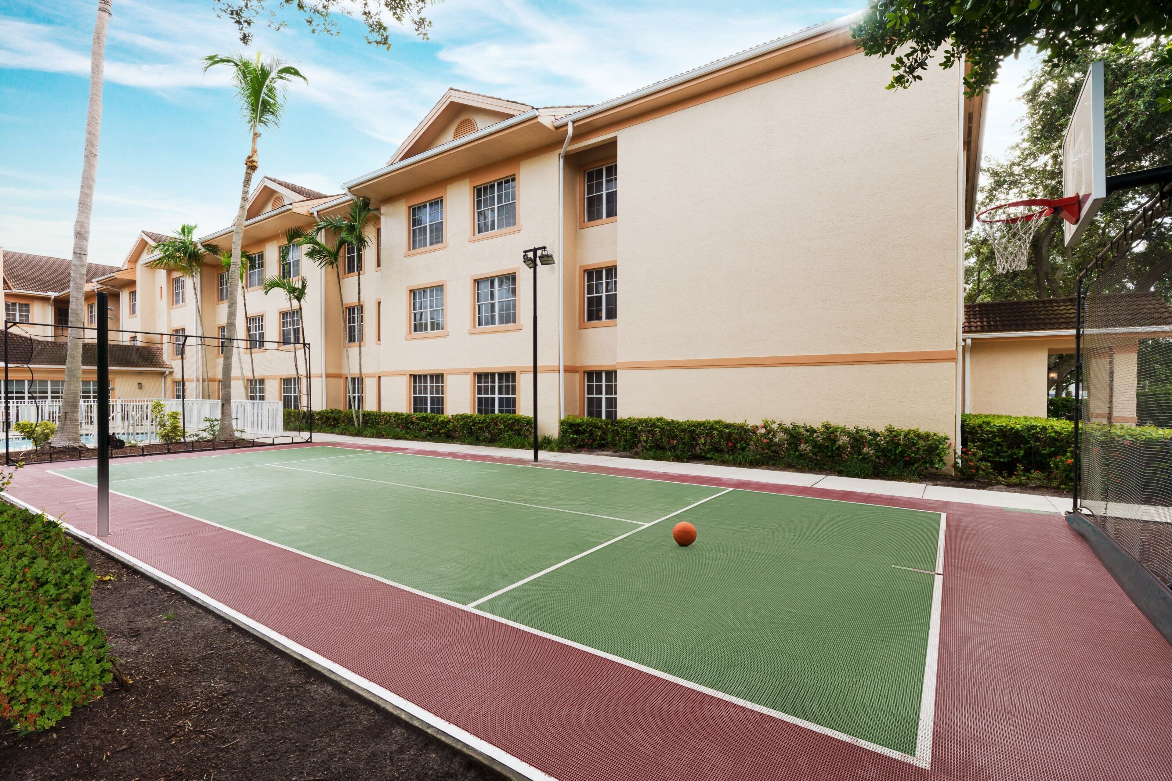Un terrain de basket en plein air, situé à côté d’un bâtiment doté de nombreuses fenêtres et d’un panier de basket.
