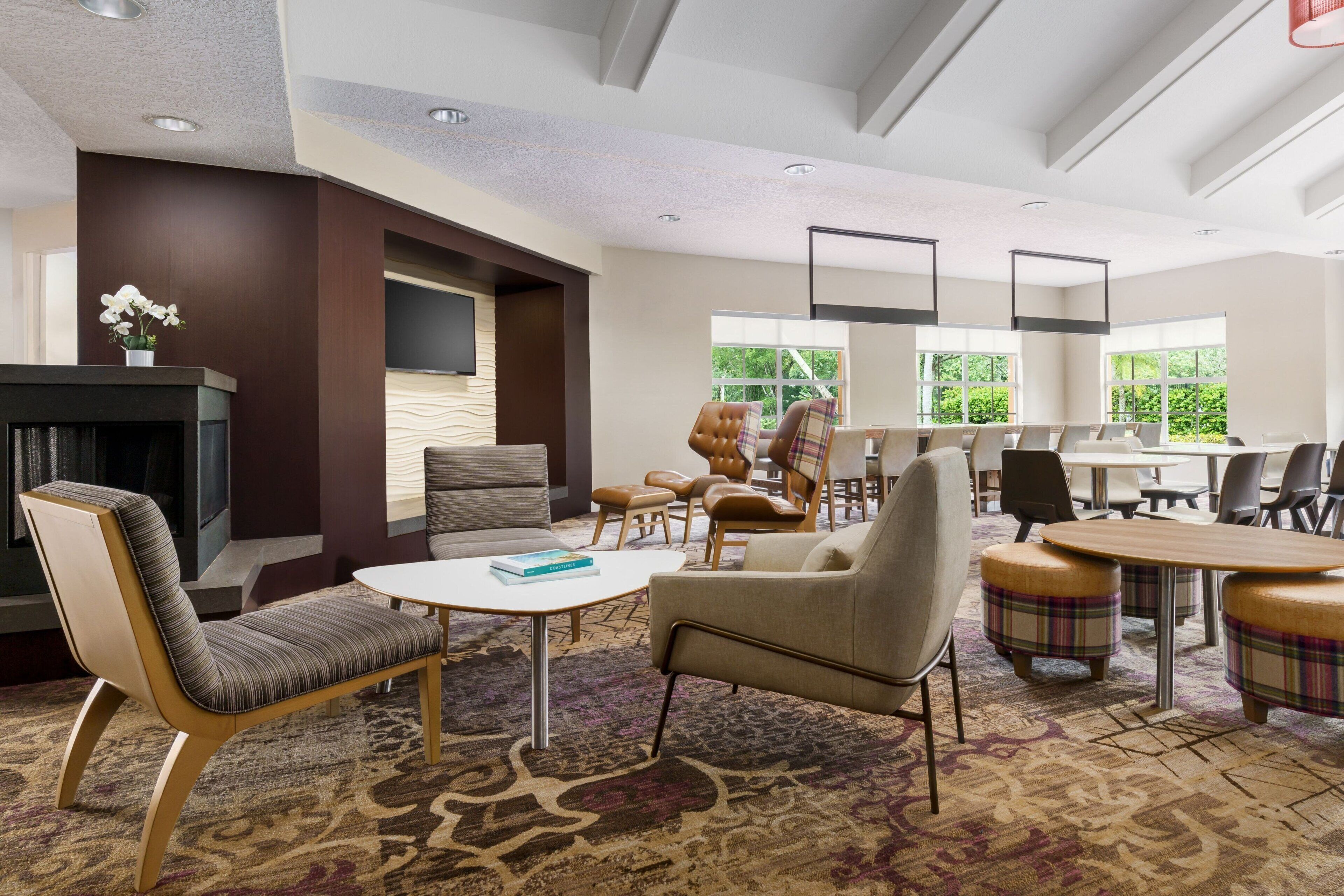 A modern hotel lobby with a fireplace, comfortable seating, a large window, and a conference table.