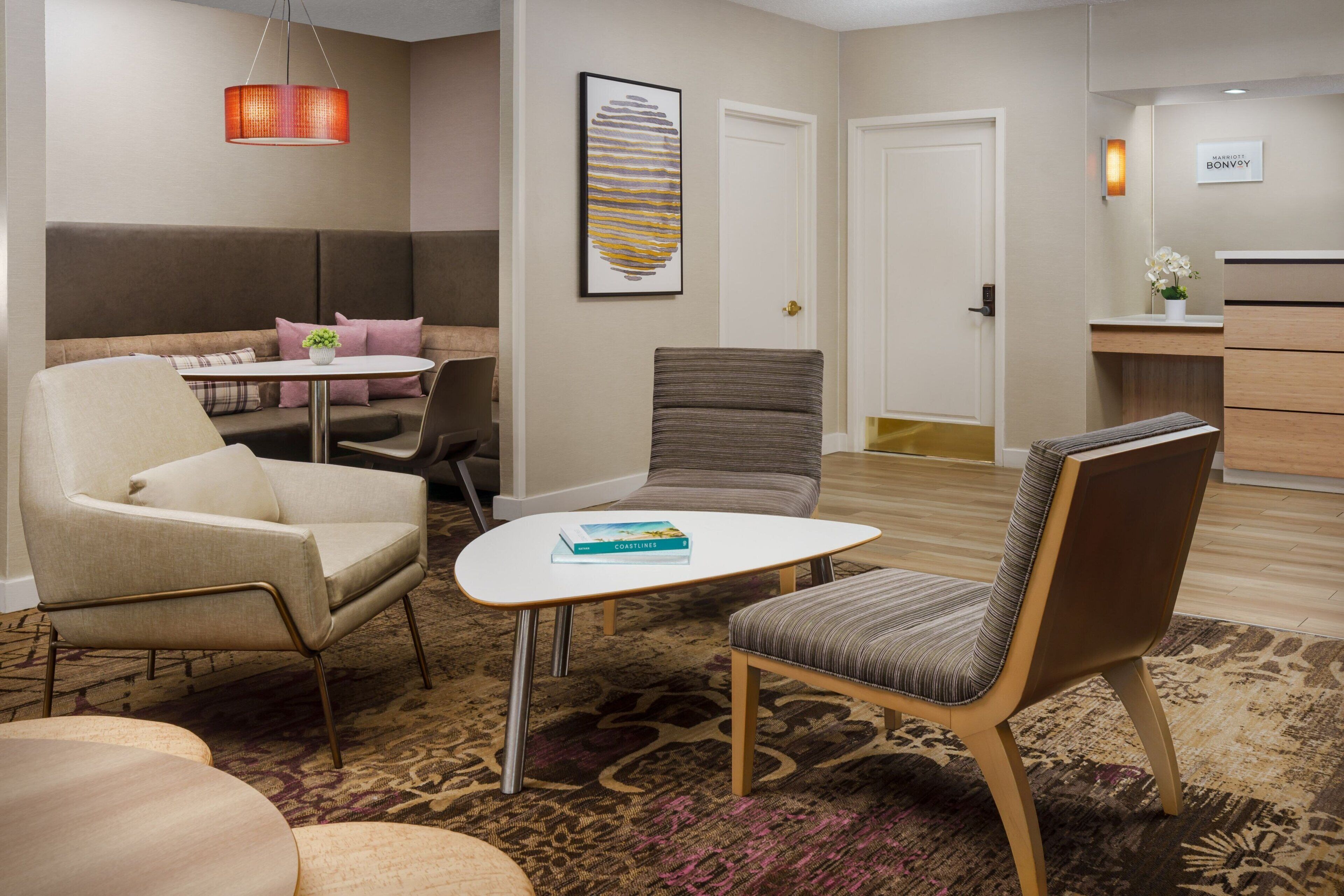 Un moderno vestíbulo de hotel con un sofá, sillones, una pequeña mesa con un libro, una alfombra estampada y una recepción.