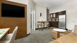 A modern hotel room with a flat-screen TV, a dining area with a table and chairs, a kitchenette with a refrigerator and microwave, and a sofa. - Residence Inn by Marriott West Palm Beach (West Palm Beach)