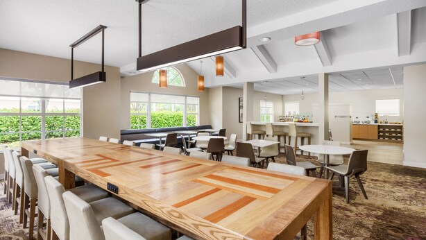 A spacious conference room with a large wooden table, multiple chairs, and a kitchen area in the background. - Residence Inn by Marriott West Palm Beach (West Palm Beach)