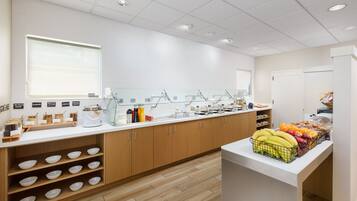 A clean, modern breakfast area with a white countertop, wooden cabinets, and a variety of food items including fruits and cereals.
