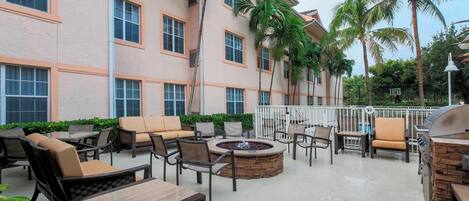 A hotel patio with outdoor seating, a fire pit, and palm trees.