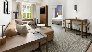 A hotel room with a sofa, a small round table, a desk with two chairs, a bed, and a TV mounted on the wall. - Residence Inn by Marriott West Palm Beach (West Palm Beach)