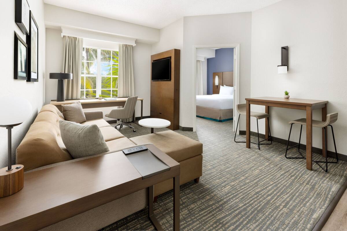Una habitación de hotel con sofá, una pequeña mesa redonda, un escritorio con dos sillas, una cama y un televisor montado en la pared.
