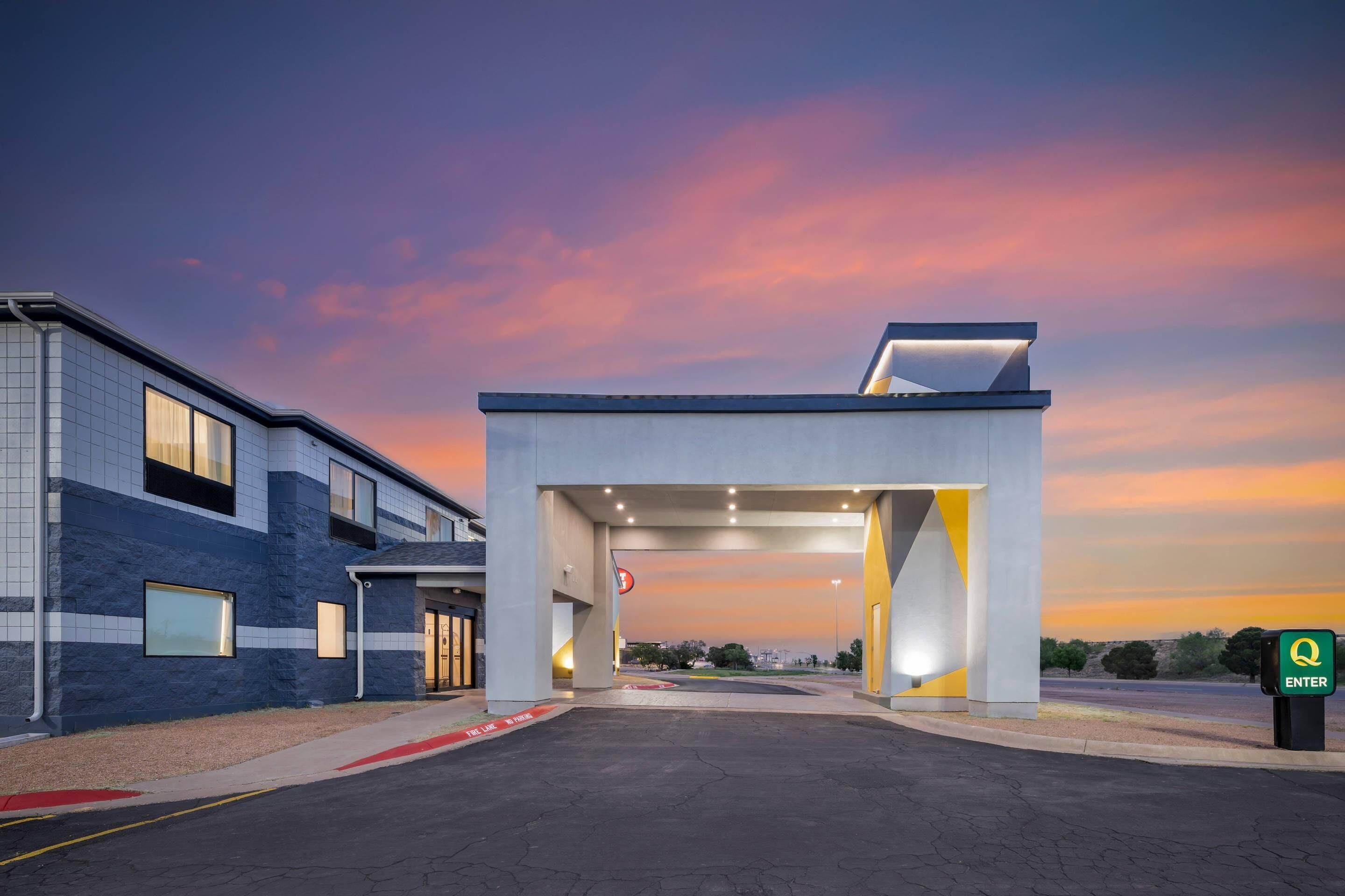 Un bâtiment moderne doté d’une entrée couverte, d’un parking et offrant une vue sur un ciel au coucher du soleil.