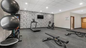Un gimnasio con equipo de ejercicio, una cinta de correr y una televisión montada en la pared.