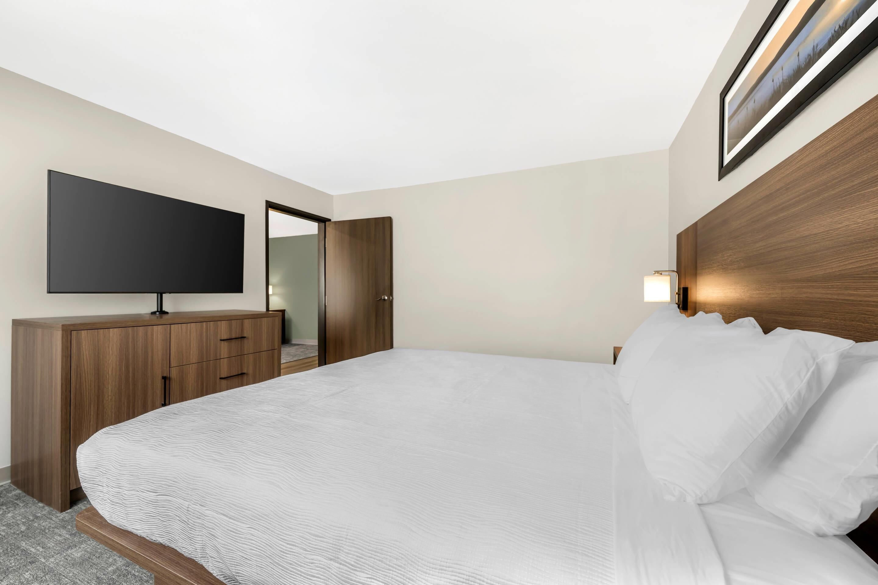 A hotel room with a large bed, a flat-screen TV, a wooden dresser, and a framed picture on the wall.
