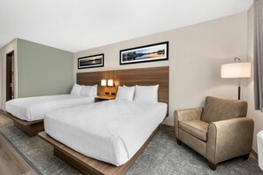 A hotel room with two beds, a sofa, a lamp, and two framed pictures on the wall.