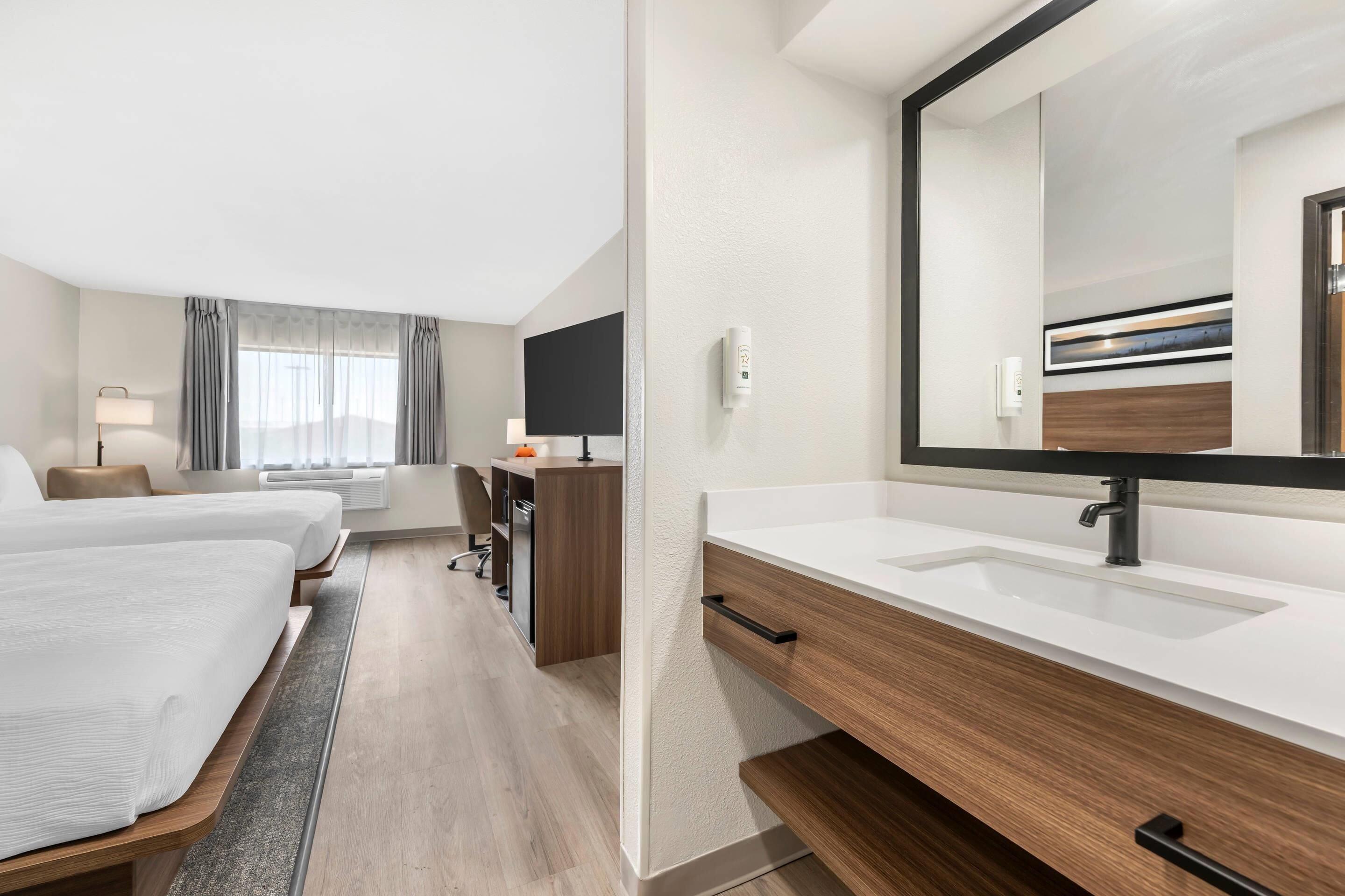 Hotelkamer met een groot bed, een bureau, een stoel, een bureaulamp, een spiegel, een wastafel en een raam met gordijnen.