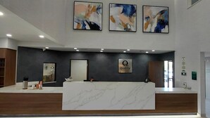 Un espace d’accueil moderne avec un comptoir en marbre, des œuvres d’art murales abstraites et un éclairage encastré.