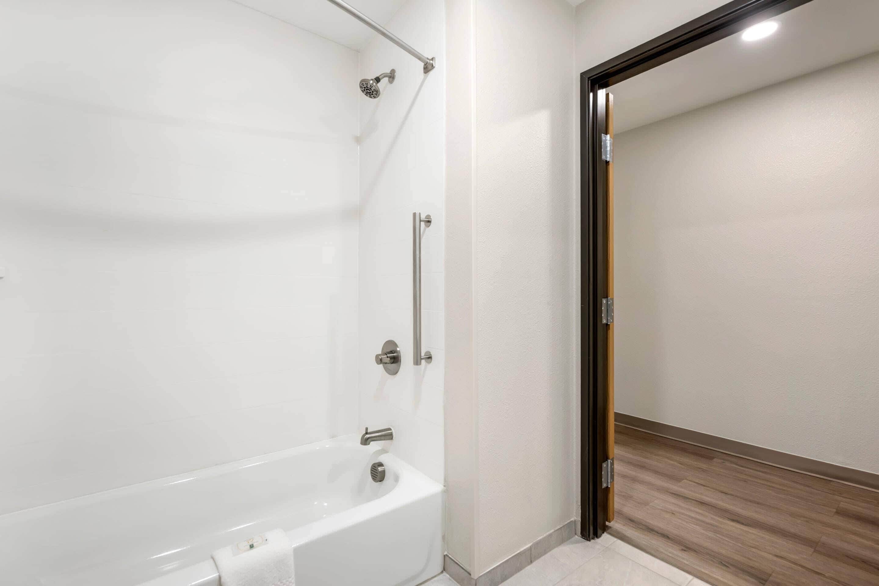 A modern bathroom with a bathtub, shower, and a wooden floor.