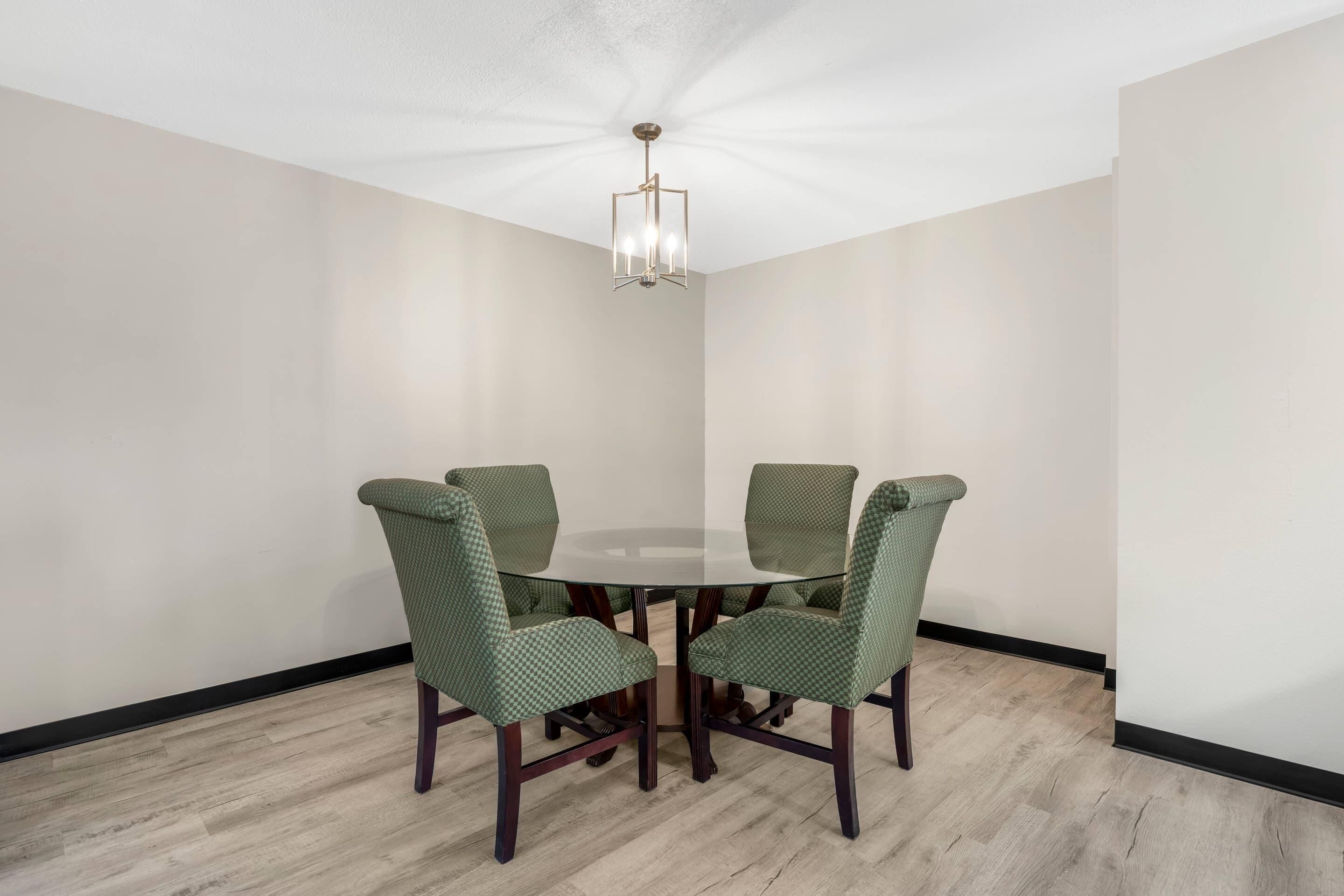 Une salle de conférence avec une table ronde, quatre chaises recouvertes d’un tissu vert, un lustre et des murs aux couleurs claires.