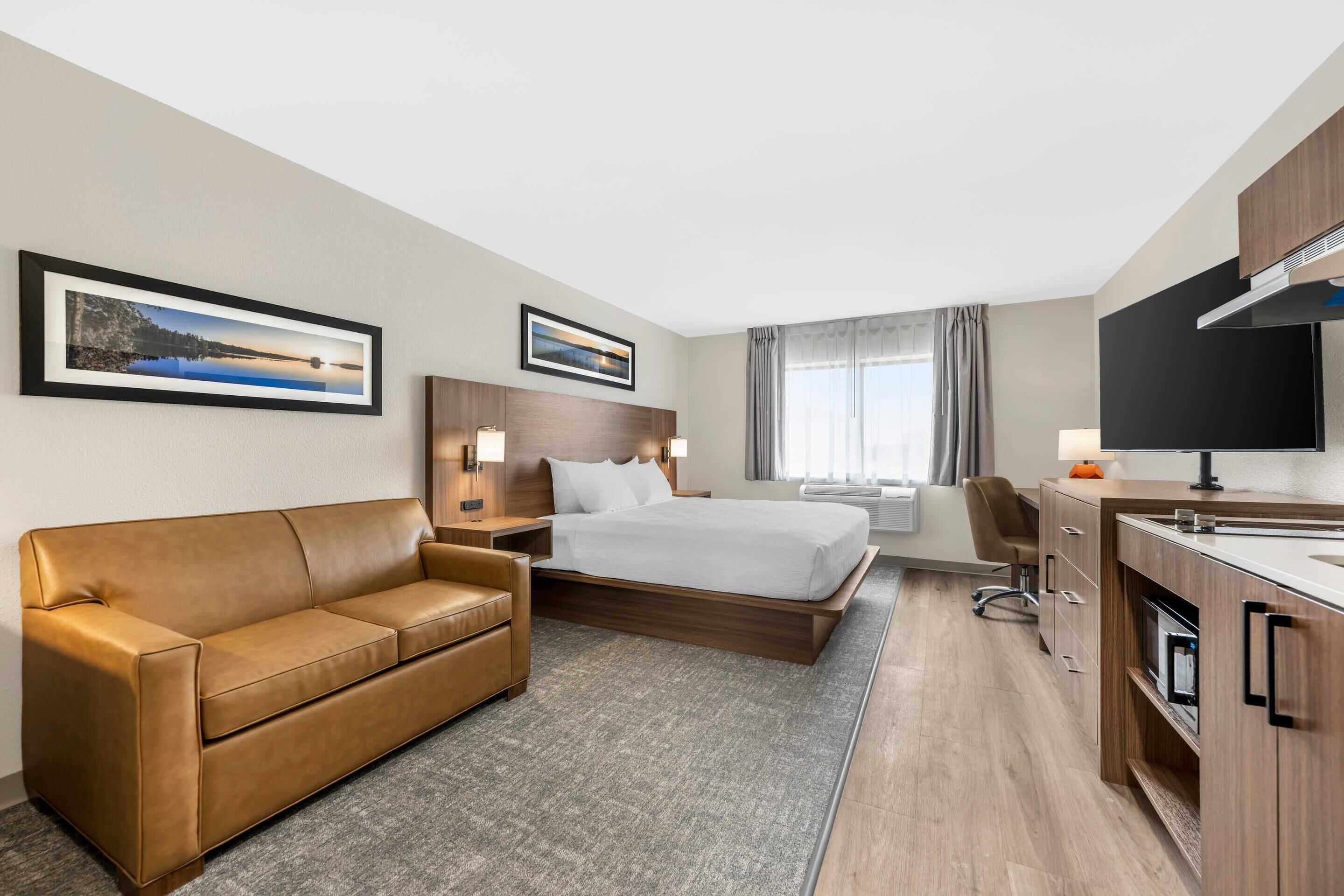 Una habitación de hotel con cama, sofá, escritorio, televisor y ventana con cortinas.