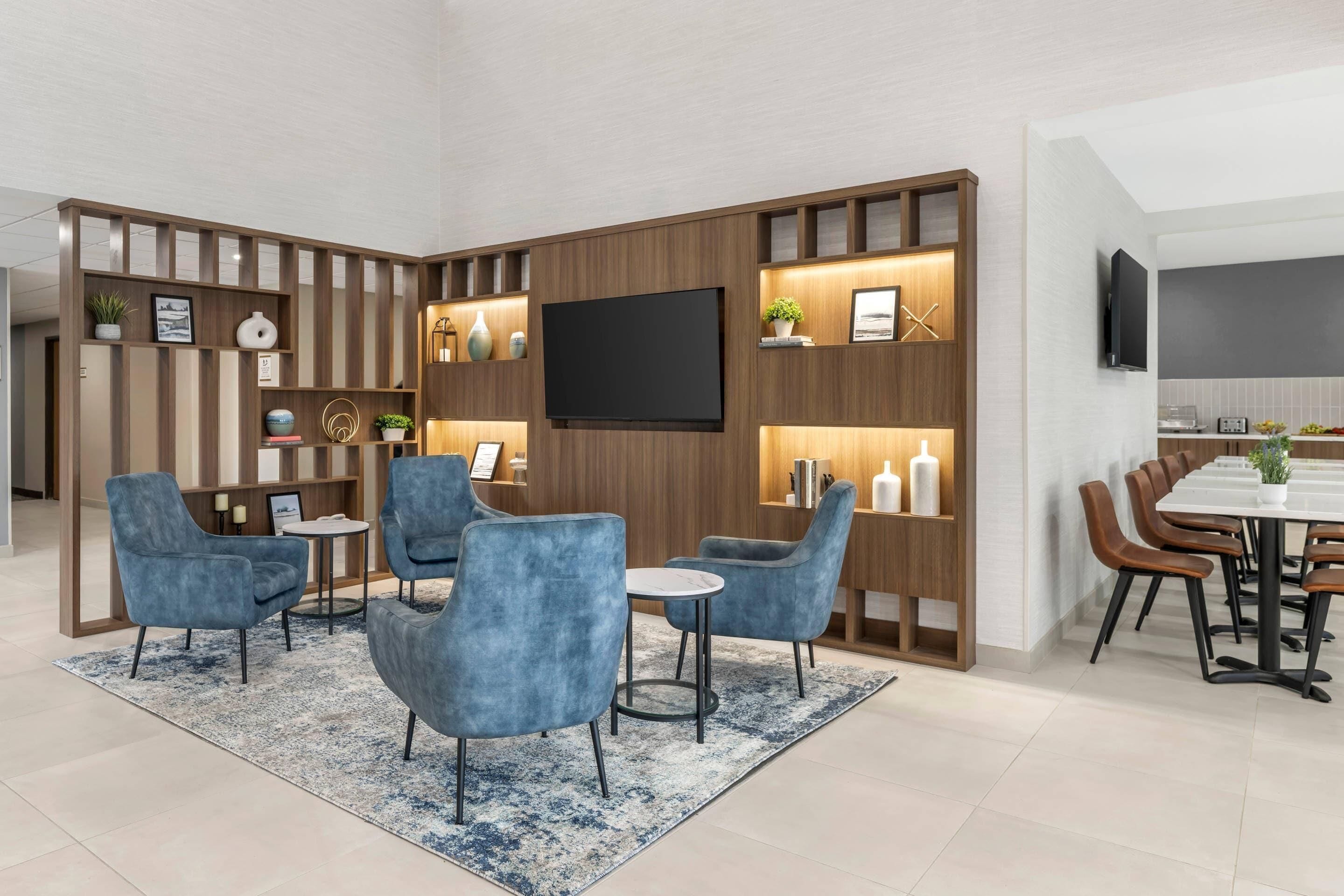 Una sala de estar moderna con televisor, sillones azules, una mesa de centro y un comedor con una mesa larga y sillas.